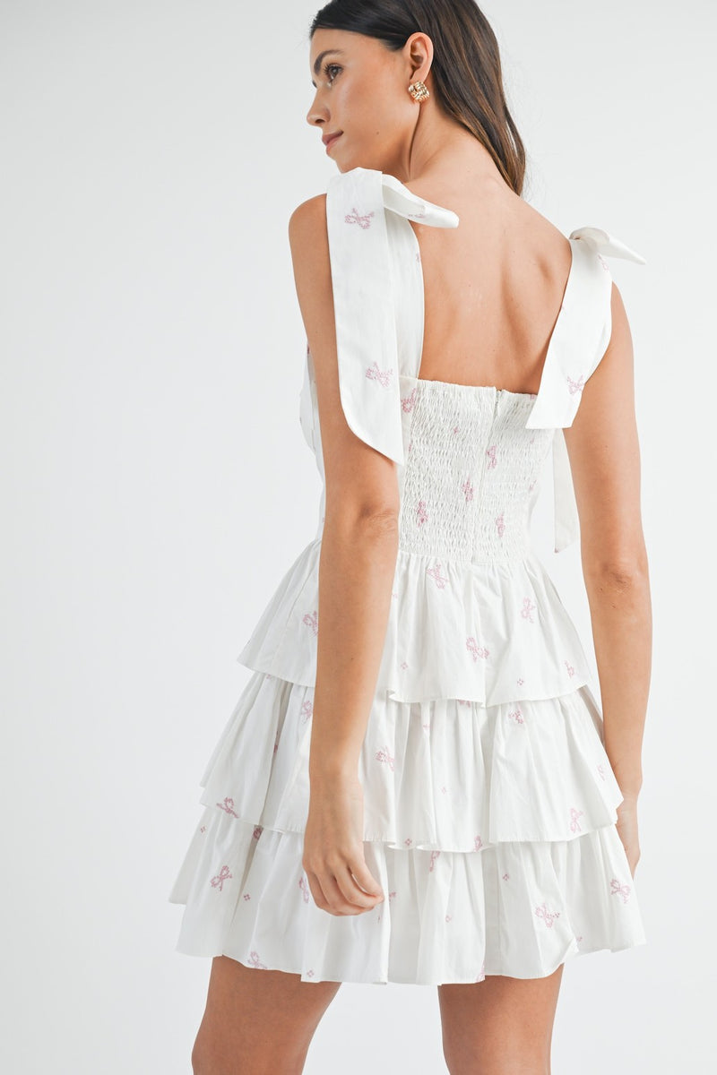 This cocktail dress features bow embroidery throughout the fabric, a sweetheart neckline with a tie in the front of the bodice and shoulder bow tie details as well. The skirt has tiered ruffle layers creating an A-line silhouette. Style this dress to make it your own at your next homecoming, sweethearts or formal event.&nbsp;    MAE MD3130B