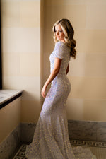 This stunning modest gown features a fitted silhouette with sequin fabric, a short sleeve and a covered back. This dress flatters the figure and offers more coverage without sacrificing style. Make this dress your own at your next prom or formal event with unique accessories and styling.   PST PS21208M