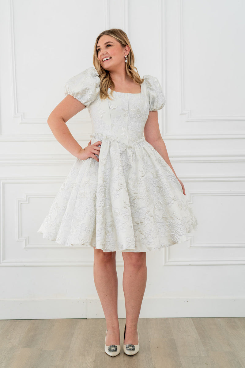 This dress features a shimmering brocade fabric that catches the light with every movement. The hidden structured boning and soft square neck provides a flattering, corset-like fit, while the full zipper back ensures effortless wear. The puff sleeves add a touch of romance, making it perfect for your next homecoming or formal event.

AG 11003