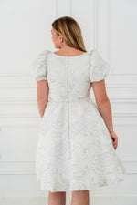 This dress features a shimmering brocade fabric that catches the light with every movement. The hidden structured boning and soft square neck provides a flattering, corset-like fit, while the full zipper back ensures effortless wear. The puff sleeves add a touch of romance, making it perfect for your next homecoming or formal event.

AG 11003