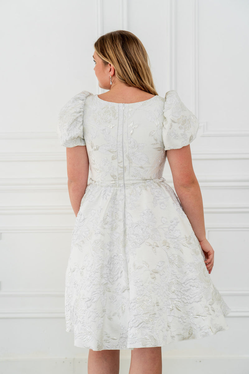 This dress features a shimmering brocade fabric that catches the light with every movement. The hidden structured boning and soft square neck provides a flattering, corset-like fit, while the full zipper back ensures effortless wear. The puff sleeves add a touch of romance, making it perfect for your next homecoming or formal event.

AG 11003
