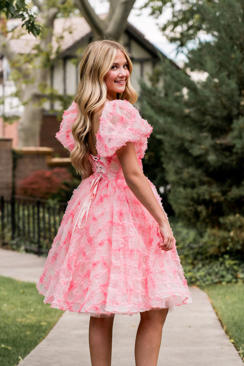 Crafted from cross-hatch tulle in dreamy watercolor pinks, this dress is a true showstopper. The structured corset top offers a universally flattering fit, the voluminous skirt is both playful and feminine, and puff sleeves complete the perfect look for your next homecoming or formal event!

AG 11001