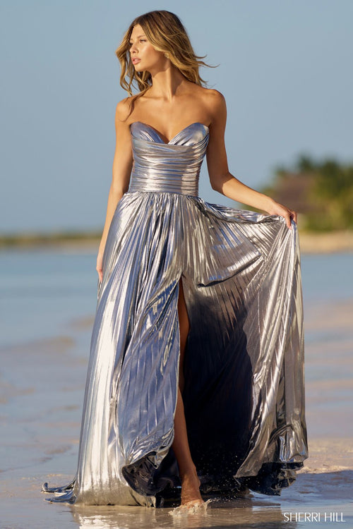 This Sherri Hill gown features pleated metallic fabric with a ruched bodice, a strapless sweetheart neckline and a skirt slit. This stunning dress could be just the vibe for your next prom or formal event!  Sherri Hill 56065