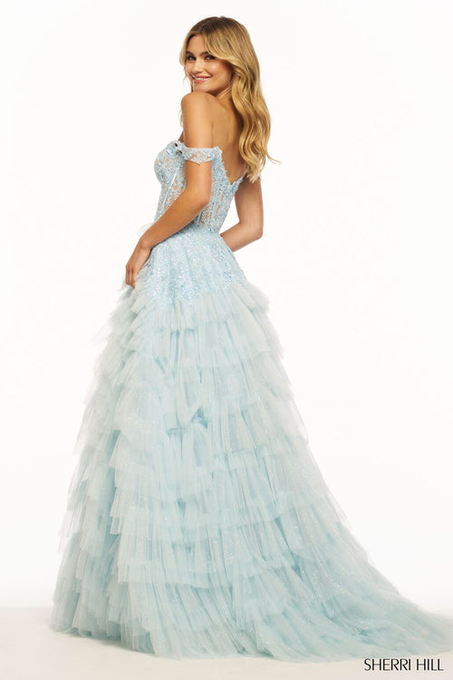 This Sherri Hill ballgown features tulle fabric with ruffle detailing, off-the-shoulder straps, a sweetheart neckline, a lace corset bodice and a skirt slit with a train to follow. This dress is a standout and could be perfect for your next prom or formal event.   Sherri Hill 56070