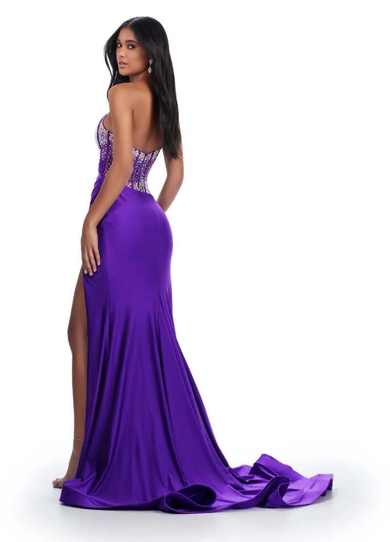 This dress features a sheer bodice with corset boning and a one shoulder neckline detailed with crystal embroidery. The fitted silhouette has a side slit and long train and jersey fabric. This dress is vibrant and could be perfect for your next prom, pageant or formal event!  Ashley Lauren 11617