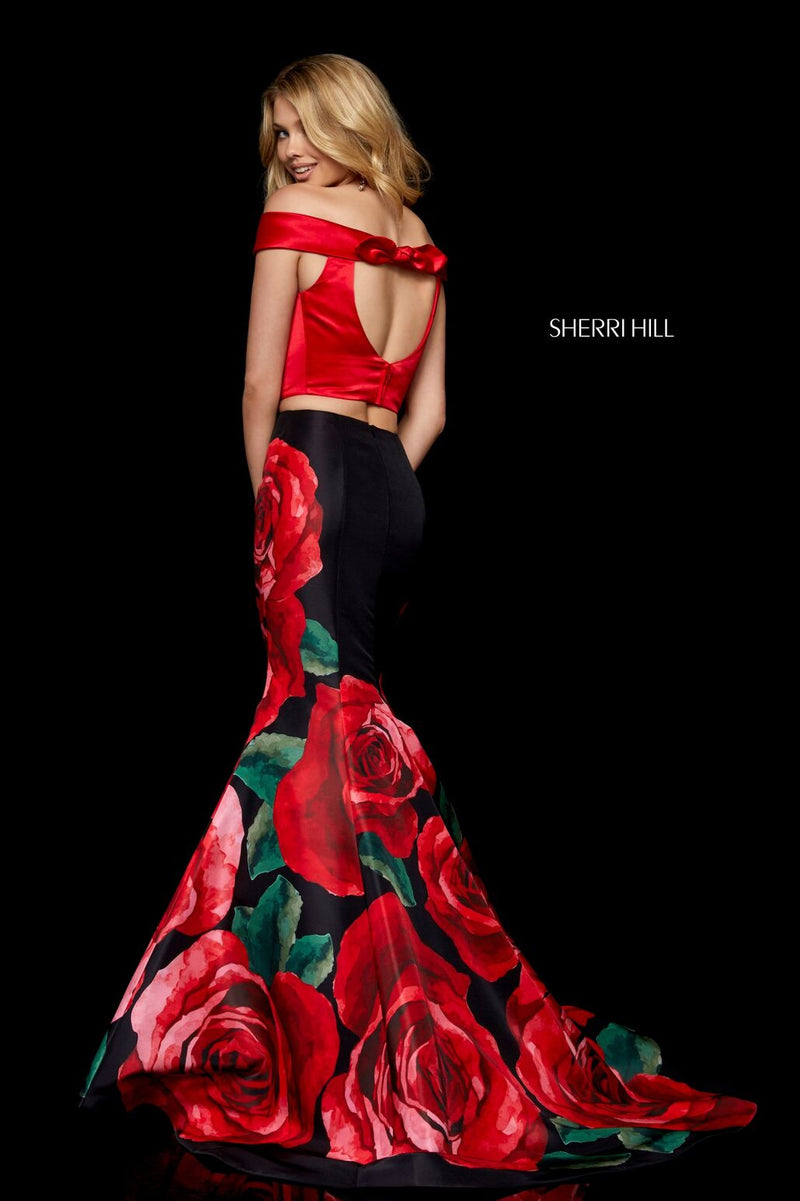 This Sherri Hill 51850 two-piece gown in red/black print features an off-the-shoulder bodice with a keyhole back and a floral mermaid skirt.