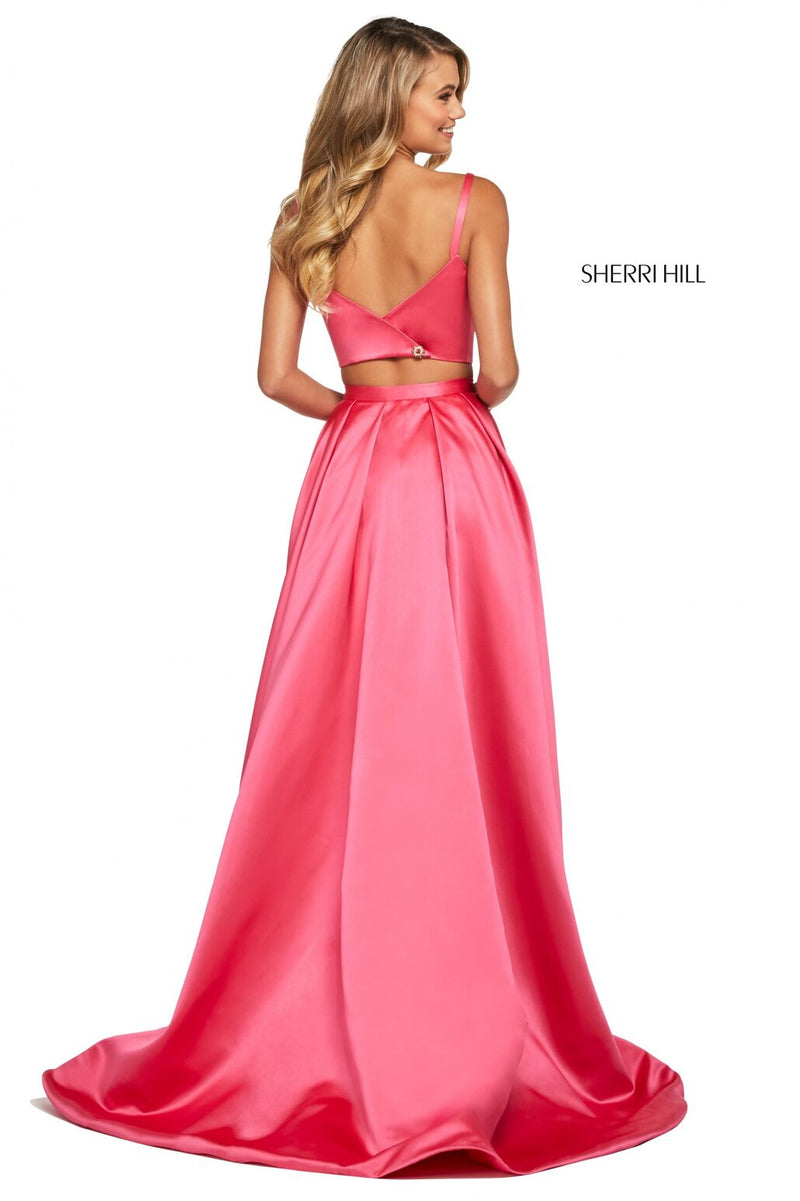 This Sherri Hill 53527 mikado two-piece gown in coral features a bateau neck bodice and a long wrap skirt with an embellished trim. 
